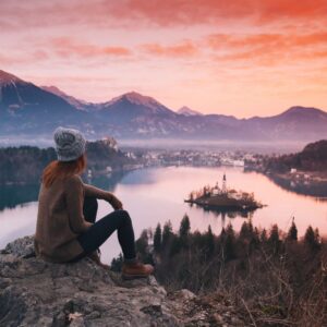 Woman sitting on top of mountain overlooking lake